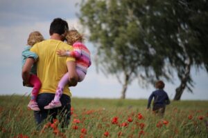 tata idący przez łąkę z córkami na rękach